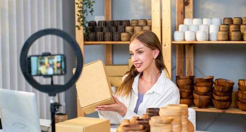 caucasian-young-woman-sell-vase-product-online-liv-2025-03-26-15-04-38-utc Caucasian young woman sell vase product online live streaming at home. Attractive girl using laptop computer shows goods to customer and present detail. Remote buying and purchase shopping concept.