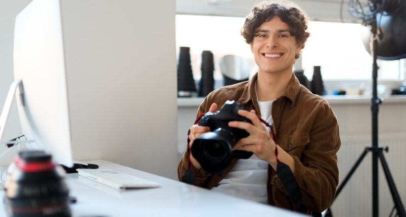 Creative job. Happy european man professional photographer working at photostudio, using digital camera and pc Creative job. Happy european man professional photographer working at photostudio, using digital camera and pc, checking photo shoot and smiling, copy space