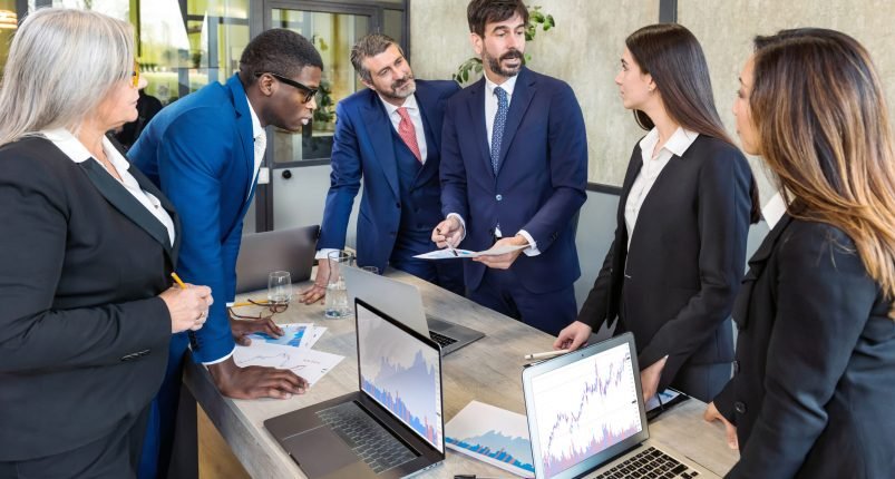 Diverse business team brainstorming in boardroom Group of multiracial colleagues in formal wear discussing graphs and planning work while gathering around table during meeting in modern office