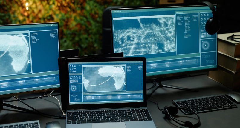 Two computer monitors and laptop with information from cameras on screens Two computer monitors and laptop with information on screens standing on workplace of officer from command and control center
